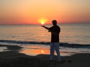 über dem Meereshorizont aufgehende Sonne hinter geöffneter Hand